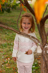 Adorable baby girl playing in a sunny park under a tree with yellow leaves, hiding behind tree