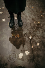 Girl in a coat, black shoes and with an umbrella. Autumn weather in the city, rain, reflection on the pavement. Drops of rain, fallen leaves.