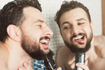 Man with razor machine cuts his beard