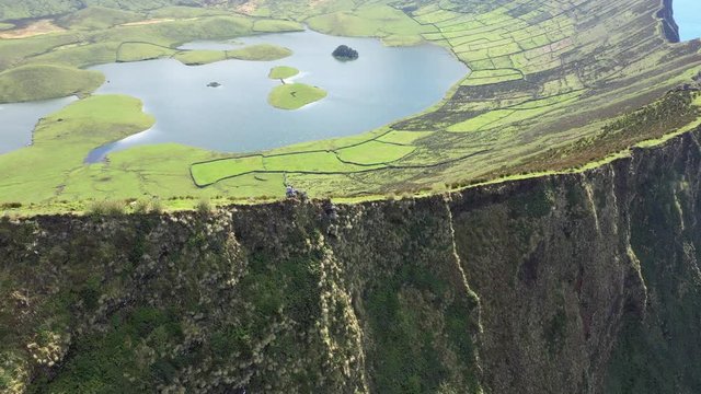 Couple on the edge of steep cliff of huge caldera. Aerial of Caldeirao volcano, Corvo, Azores