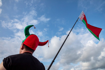A fan in a cap of the colors of the Belarusian flag and with the national flag of the Republic of Belarus is walking down the street