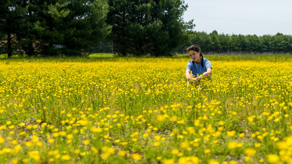 Fototapeta premium Teen girl sitting in large field with yellow flowers and trees in the background