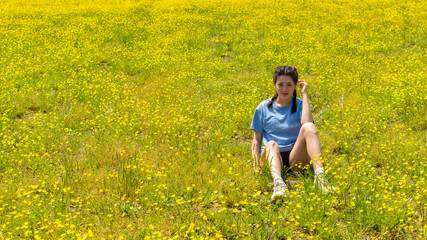 Teen girl with braids sitting in large field with yellow flowers