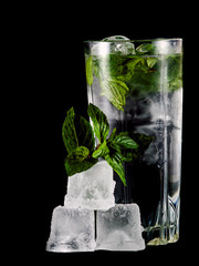 A glass of cold water, ice cubes and mint leaves on a black background.