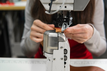 Sewing machine in a leather workshop in action with hands working on a leather details for shoes. Women's hands with sewing machine at shoes factory.