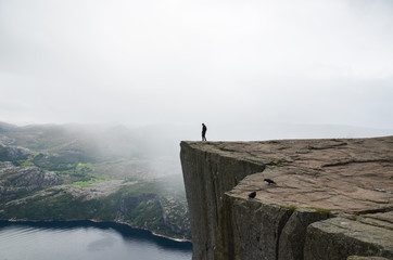 A man standing on the edge of the cliff Preikestolen in Norway. Moody summer weather and beautiful...