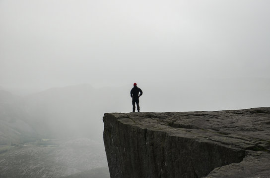A man standing on the edge of the cliff Preikestolen in Norway. Moody summer weather and beautiful scenery. 