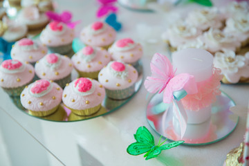 Cake in the background . Artificial pink and green butterfly on white candle.