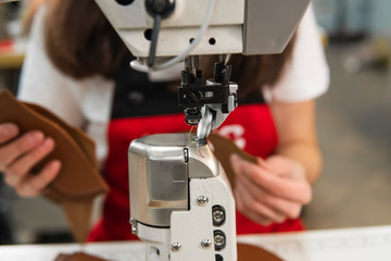 Sewing machine in a leather workshop in action with hands working on a leather details for shoes. Women's hands with sewing machine at shoes factory.