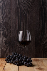 Wine bottle and a glass of wine. A bunch of ripe black grapes. Wooden background.