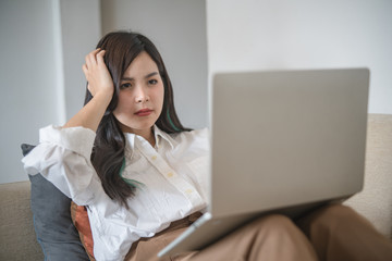 Serious woman using laptop and sitting on sofa.