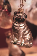 Cute pug dog Christmas ornament closeup on blurry background. Retro style shiny glass Christmas decoration with shiny pearly golden surface. Winter holiday attribute. New Year celebration decor