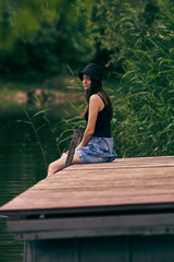 girl in panama hat posing on a pier by a lake in the woods