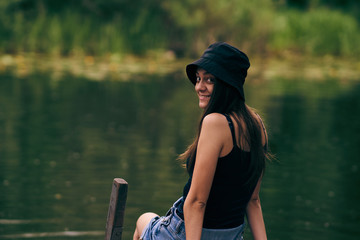 girl in panama hat posing on a pier by a lake in the woods