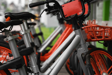 Street transportation orange hybrid rent bicycles with electronic form of payment for traveling around the city stand in row on rental network parking lot waiting for cyclists to make bike trip.