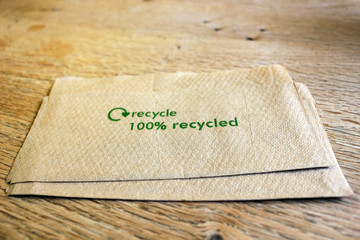A paper napkin with the words 100% recycled on a wooden table