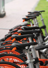 Street transportation orange hybrid rent bicycles with electronic form of payment for traveling around the city stand in row on rental network parking lot waiting for cyclists to make bike trip.