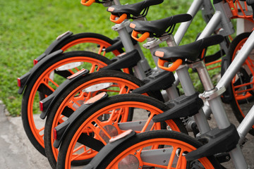 Street transportation orange hybrid rent bicycles with electronic form of payment for traveling around the city stand in row on rental network parking lot waiting for cyclists to make bike trip.