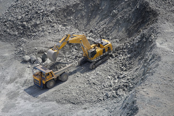 Excavator loads ore into a large mining dump truck. Open pit. Top view