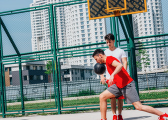 Two friends play basketball in the middle of the day on the court