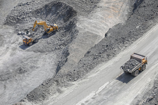 Excavator loads ore into a large mining dump truck. Open pit. Top view
