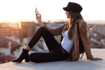 Pretty young woman taking a selfie with mobile phone while sitting on the rooftop.