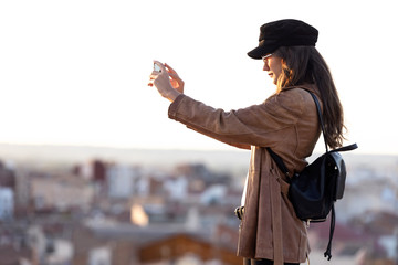 Pretty young woman taking photographs of sunset on the rooftop.