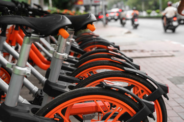 Street transportation orange hybrid rent bicycles with electronic form of payment for traveling around the city stand in row on rental network parking lot waiting for cyclists to make bike trip.