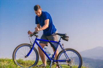 Obraz premium Fit male mountain biker pushing his bike uphill while looking exhausted on a sunny summer day.