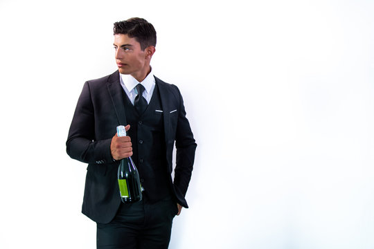 Good looking man in suit holding bottle of sparkling wine in front of white wall with plenty of room for copy