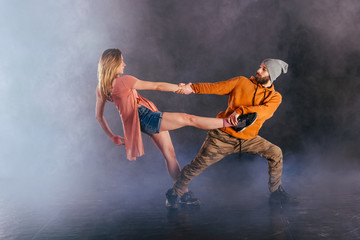 Couple dancing modern dance and showing off their leg stretch moves.Black background while the couple is dressed in urban colorful clothes...
