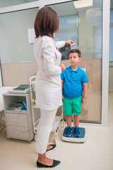 Female doctor measuring the height of little boy in a clinic ( hospital ) while smiling and being gentle.