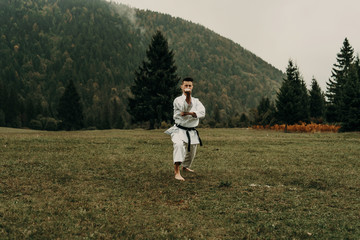 Fototapeta na wymiar Martial art of karate, a man in a kimono with black belt trains on the mountain,free space.