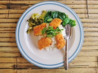 Steamed rice topped with fried crispy fish placed on a bamboo table