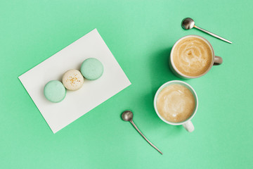 Fototapeta na wymiar Fashion flat lay with two cup of coffee and tasty macaroons on trend color mint background with copy space. Sweet food and hot cappuccino in big mug. Winter Morning concept. Top view.
