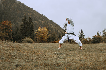 Martial art of karate, a man in a kimono with black belt trains on the mountain,free space.