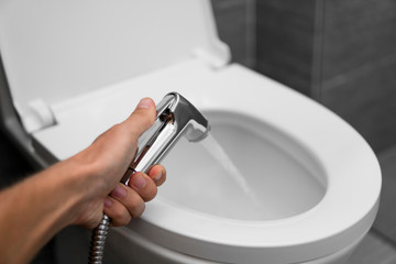 Using of bidet shower with a white toilet. Bidet shower in male hand for using with a white toilet bowl.