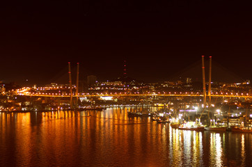 The bridge over the Golden Horn in Vladivostok and the lights of the night city reflected in the water.