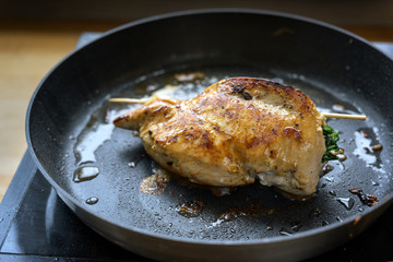 stuffed chicken breast fillet with spinach filling sizzles while frying in a pan on the stove