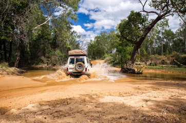 Fototapeta na wymiar Western Australia – Flooded Outback gravel road with 4WD car crossing the waterhole with splashing muddy water at the savanna