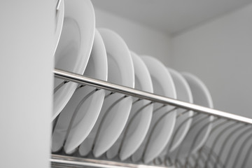 Dish drying metal rack with big nice white clean plates. Traditional comfortable kitchen. Open white dish draining closet with wet dishes of glass and ceramic, plates, bowls drying inside on rack.