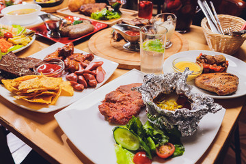 Dining table with a variety of snacks and salads. Salmon, olives, wine, vegetables, grilled fish...