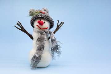Toy snowman on a blue background. Snowman in a gray knitted hat and with a gray scarf. Place for text
