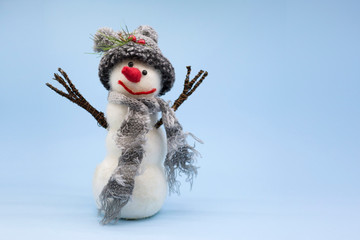 Toy snowman on a blue background. Snowman in a gray knitted hat and with a gray scarf. Place for...