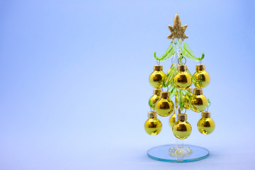 Christmas atmosphere props. Miniature model winter pine tree with golden balls on a blue background. New Year card. Place for text