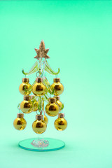 Small model winter pine tree with golden balls on a green background. New Year card. Christmas atmosphere props