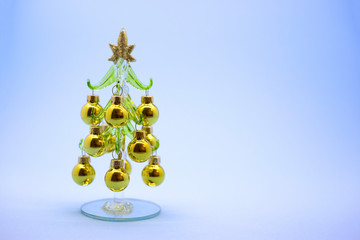 Miniature model winter pine tree with golden balls on a blue background. New Year card. Place for text. Christmas atmosphere props. 