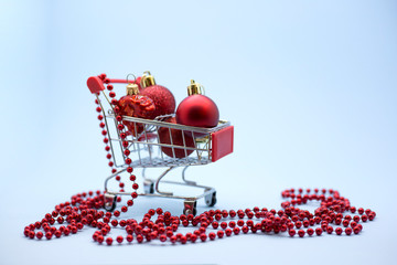 Miniature model shopping trolley with Сhristmas balls inside on a blue backgound. Christmas sales and discounts concept