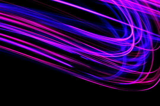 Long exposure photograph of pink and purple neon colour in an abstract swirl, parallel lines pattern against a black background. Light painting photography.
