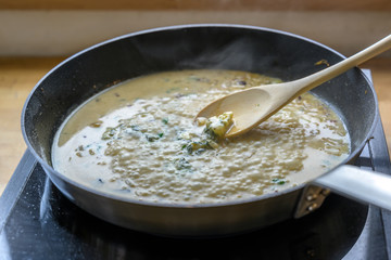 boiling gorgonzola cheese sauce in the pan on a mobile stove is stirred with a wooden spoon,...